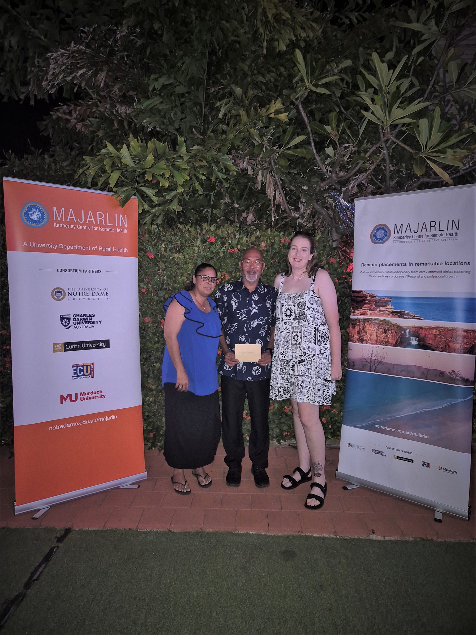 Vaughan Matsumoto with two family members at a celebration ceremony, holding a gold envelope.